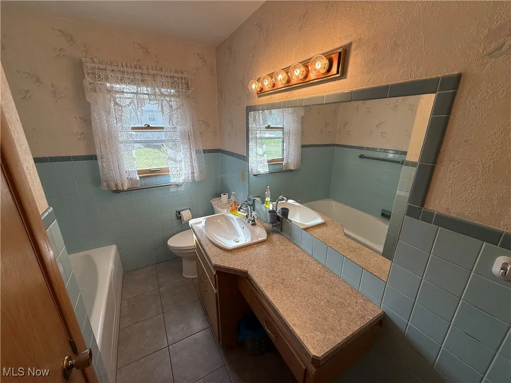 Bathroom featuring tile walls, vanity, tile patterned flooring, toilet, and a washtub