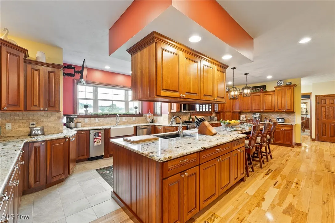 Kitchen with sink, a center island with sink, light hardwood / wood-style floors, decorative light fixtures, and light stone countertops