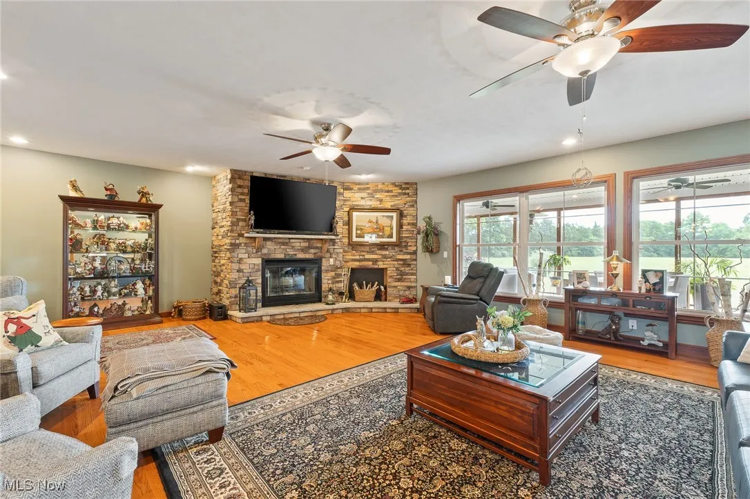 Living room with hardwood / wood-style floors, a stone fireplace, and ceiling fan