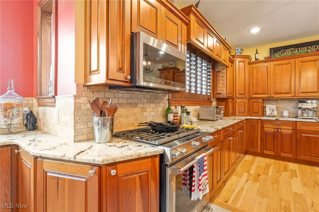 Kitchen with light stone countertops, light wood-type flooring, stainless steel appliances, and tasteful backsplash