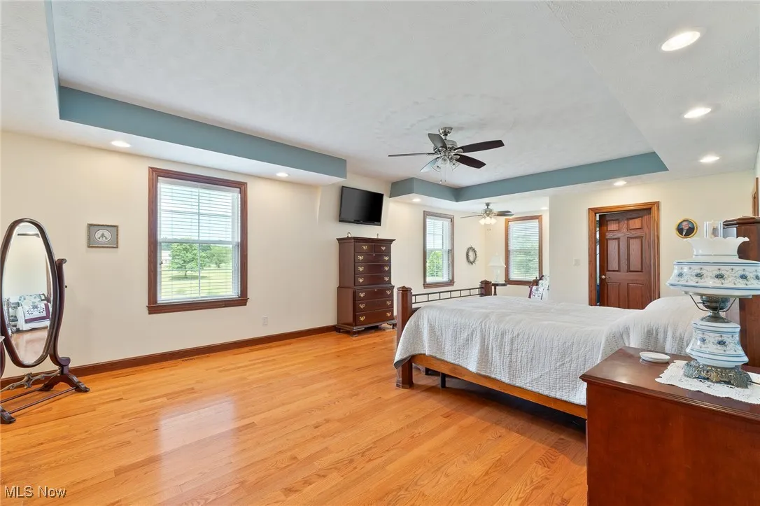 Bedroom with baseboard heating, ceiling fan, a tray ceiling, and light hardwood / wood-style floors