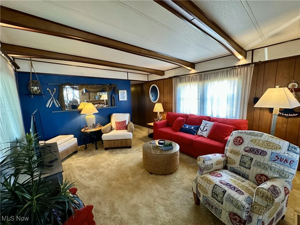 Carpeted living room with wood walls, beamed ceiling, and a textured ceiling