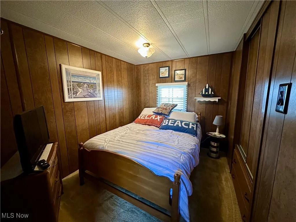 Carpeted bedroom with wooden walls and a textured ceiling