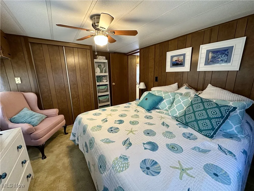 Bedroom featuring a closet, wooden walls, light colored carpet, and ceiling fan