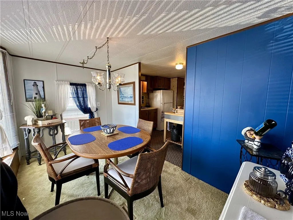 Carpeted dining space featuring wood walls, a notable chandelier, and a textured ceiling