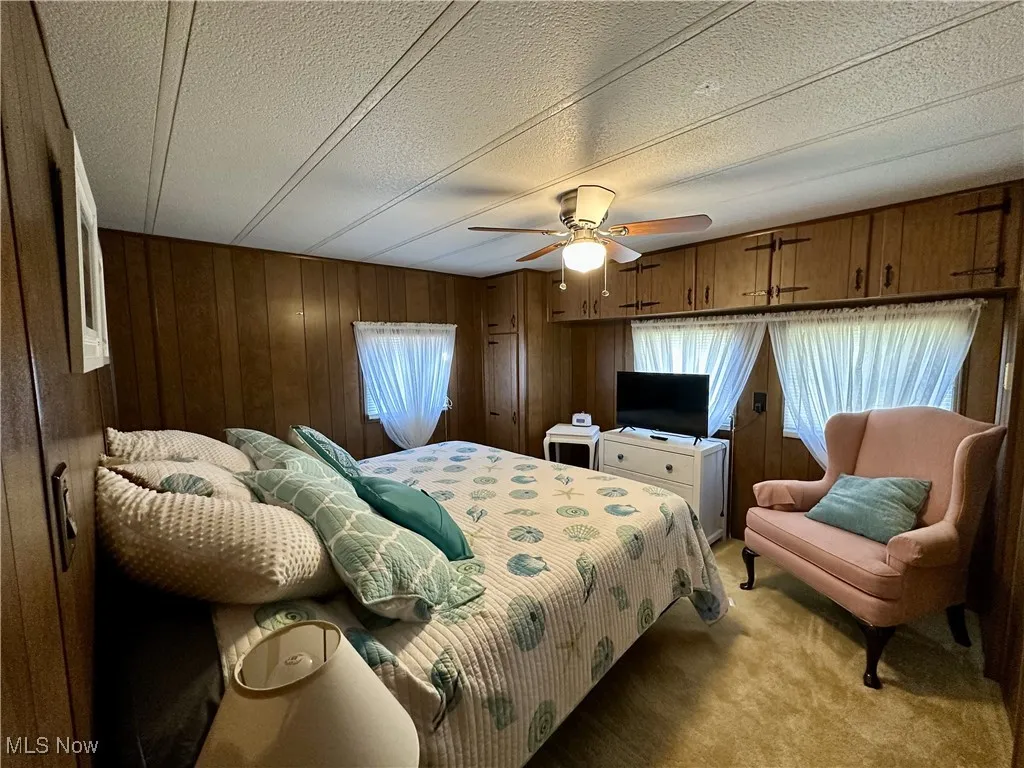 Bedroom with carpet floors, a textured ceiling, wood walls, and ceiling fan