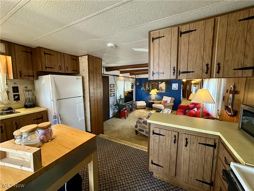 Kitchen with dark carpet, white refrigerator, a textured ceiling, stove, and wooden walls