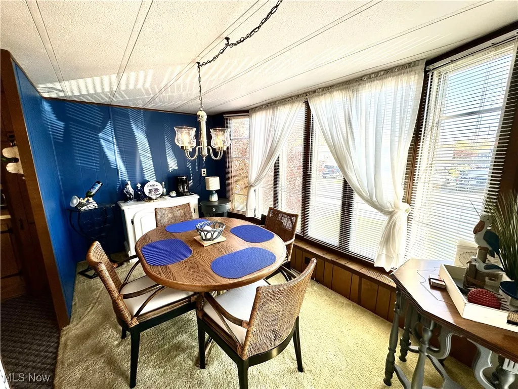 Dining space featuring carpet flooring, wood walls, a textured ceiling, and a chandelier