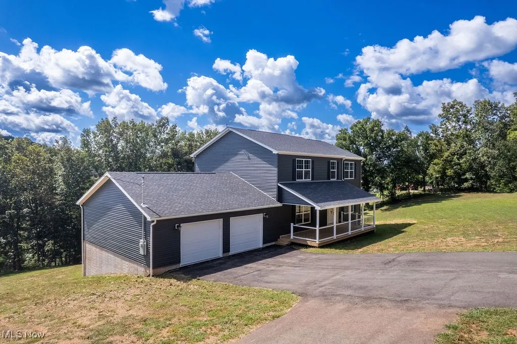 View of front facade with a front yard, a shingled roof, covered porch, driveway, and a garage