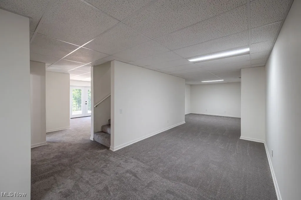 Carpeted spare room with stairs and a paneled ceiling