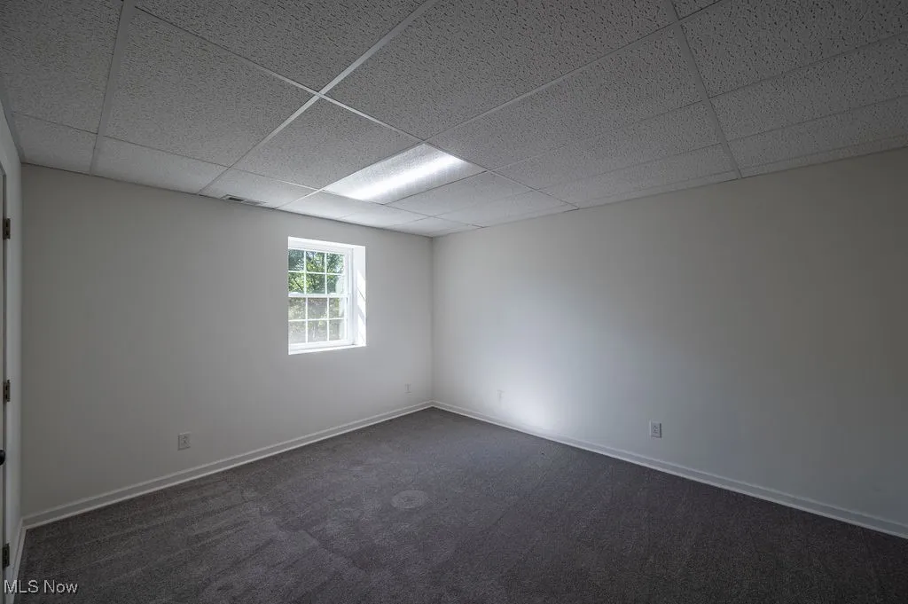 Unfurnished room with dark colored carpet and a paneled ceiling