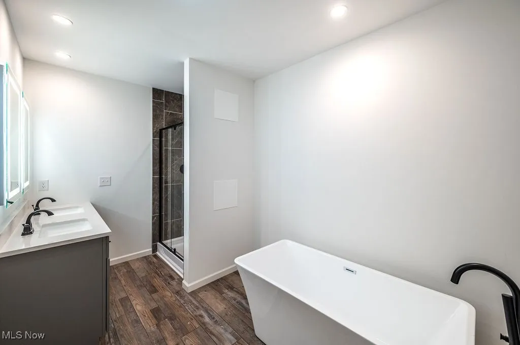 Full bath with a soaking tub, double vanity, dark wood-style floors, a stall shower, and recessed lighting