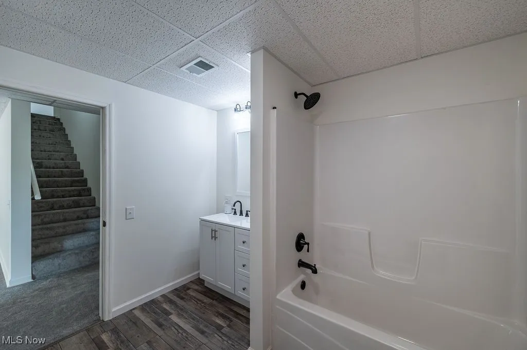 Full bath with tub / shower combination, vanity, dark wood-type flooring, and a paneled ceiling