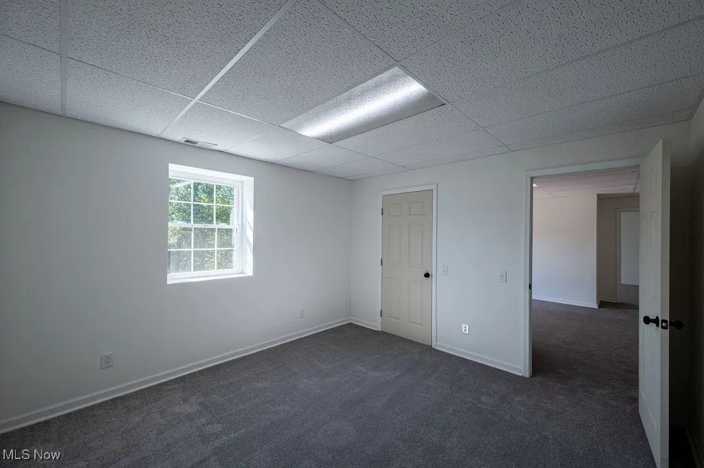 Unfurnished room with dark colored carpet and a paneled ceiling
