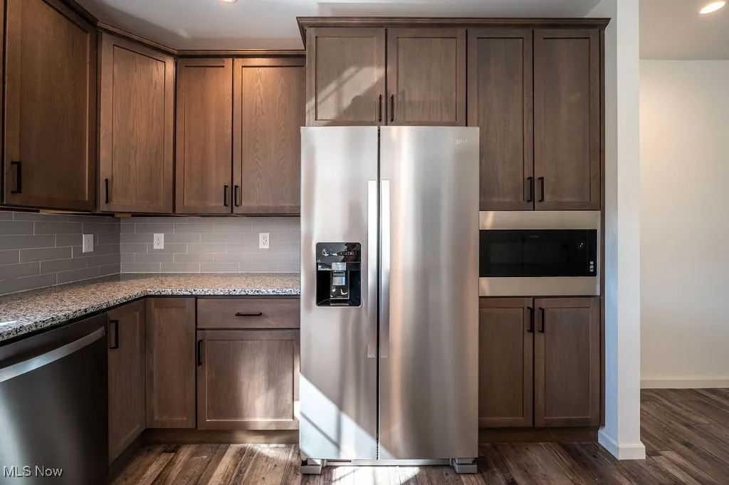 Kitchen featuring appliances with stainless steel finishes, light stone countertops, dark wood-style flooring, backsplash, and recessed lighting