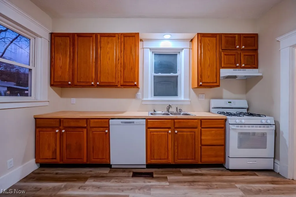 Kitchen with white appliances, light hardwood / wood-style floors, and sink
