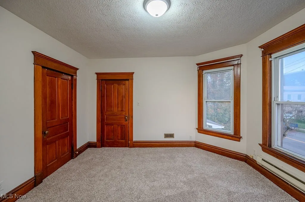 Unfurnished bedroom featuring carpet flooring, a textured ceiling, and a baseboard heating unit