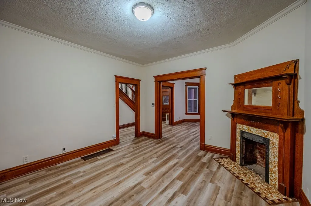 Unfurnished living room featuring crown molding, a textured ceiling, and light hardwood / wood-style flooring
