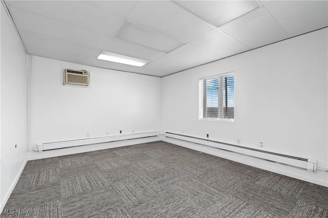 Spare room with dark colored carpet, an AC wall unit, and a baseboard heating unit