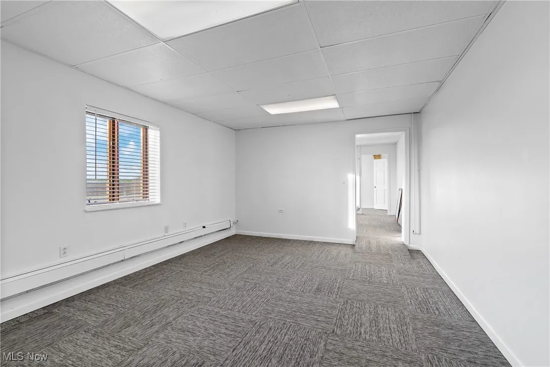 Empty room with a paneled ceiling, a baseboard radiator, and dark colored carpet