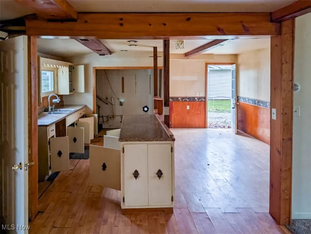 Kitchen with beam ceiling, light hardwood / wood-style floors, sink, and white cabinetry