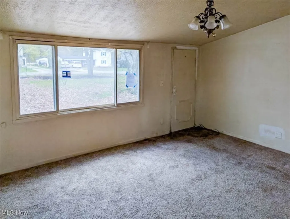 Carpeted empty room with a notable chandelier, a textured ceiling, and a wealth of natural light