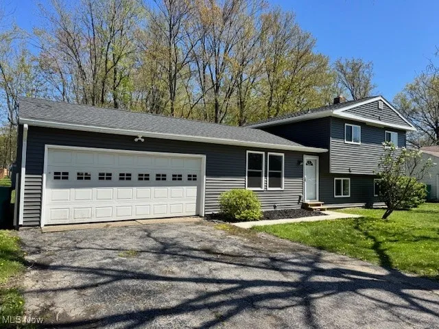 Split level home featuring asphalt driveway, an attached garage, and a front lawn
