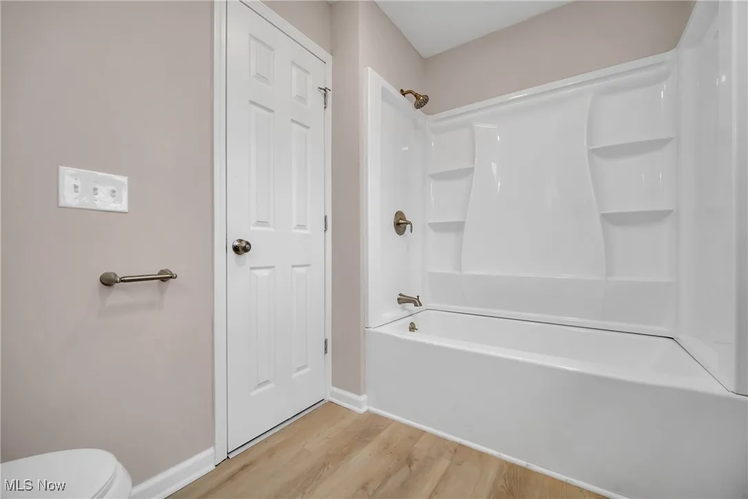 Bathroom featuring hardwood / wood-style floors, toilet, and bathing tub / shower combination