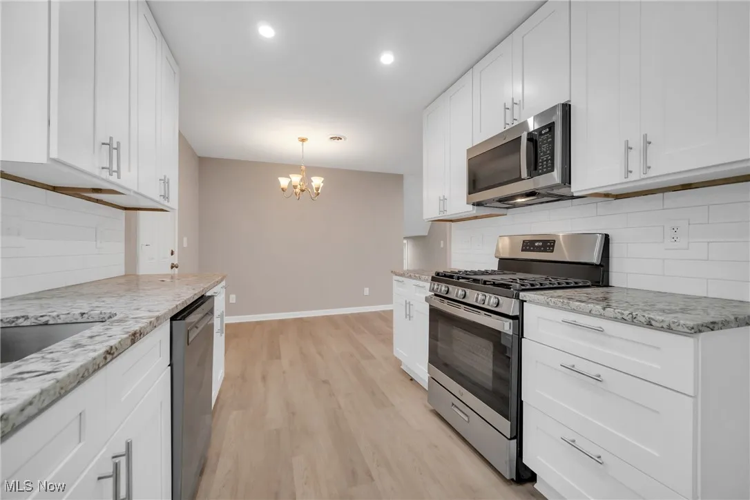 Kitchen featuring hanging light fixtures, appliances with stainless steel finishes, a chandelier, white cabinets, and light wood-type flooring