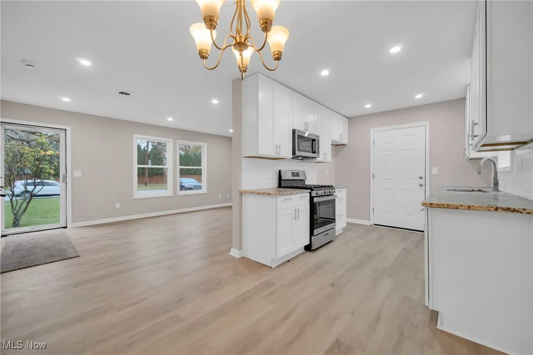 Kitchen featuring an inviting chandelier, sink, hanging light fixtures, white cabinetry, and stainless steel appliances