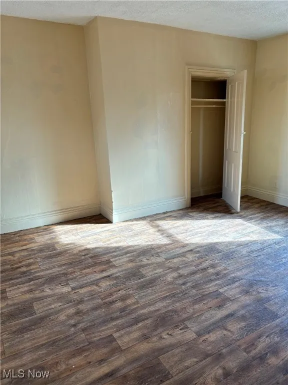 Unfurnished bedroom featuring dark hardwood / wood-style floors, a textured ceiling, and a closet