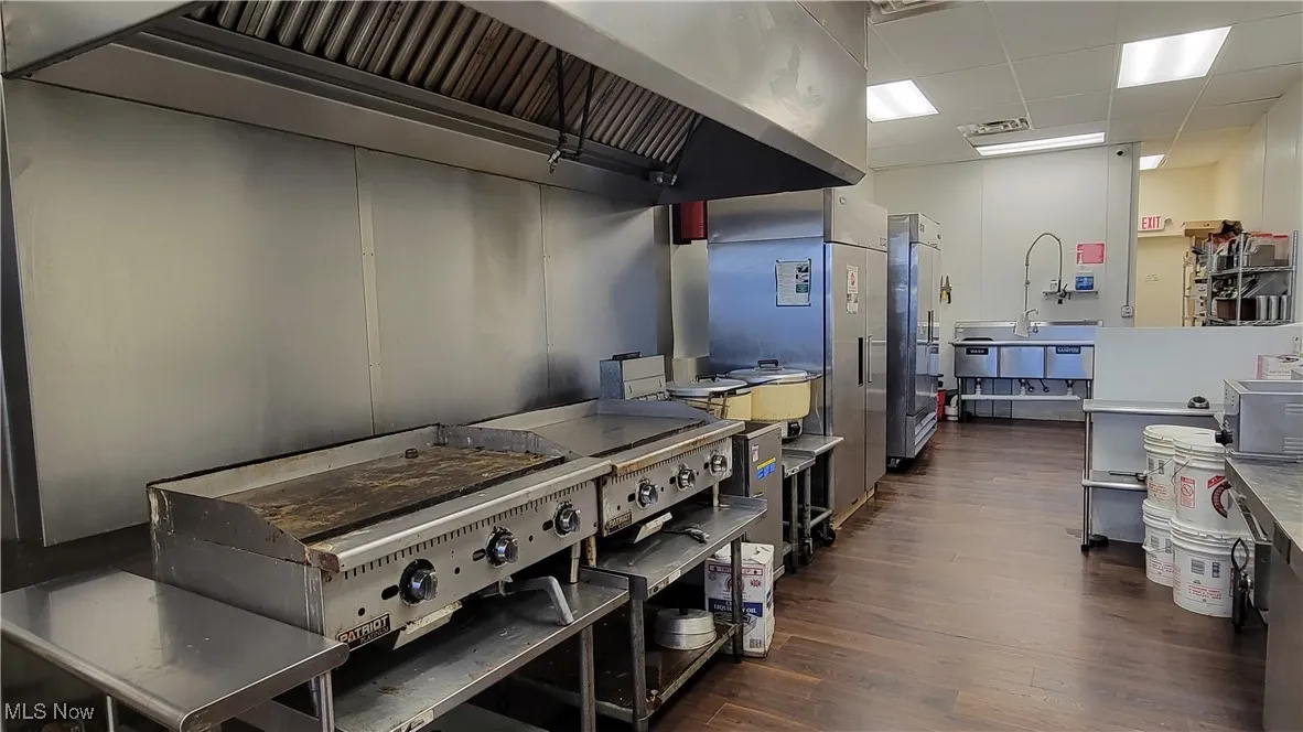 Kitchen featuring stainless steel fridge, a drop ceiling, wall chimney exhaust hood, and dark hardwood / wood-style floors
