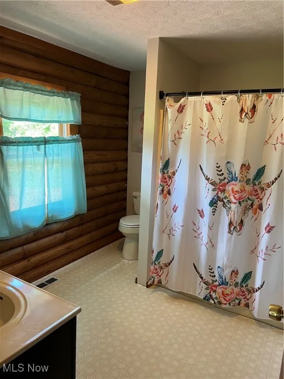 Bathroom featuring rustic walls, vanity, a textured ceiling, and toilet