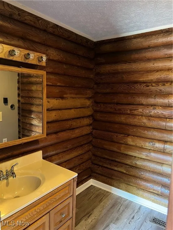 Bathroom featuring rustic walls, hardwood / wood-style floors, vanity, and a textured ceiling
