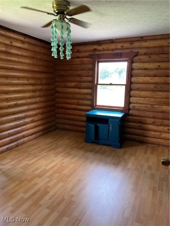 Empty room featuring hardwood / wood-style floors, a textured ceiling, rustic walls, and ceiling fan