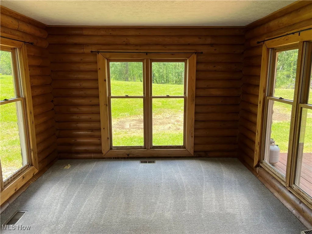 Carpeted spare room featuring log walls and a textured ceiling