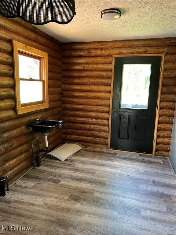 Entryway with log walls, wood-type flooring, and a textured ceiling