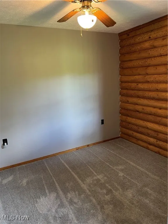 Carpeted spare room with rustic walls and a textured ceiling