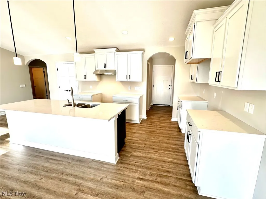Kitchen featuring a kitchen island with sink, sink, decorative light fixtures, hardwood / wood-style floors, and white cabinetry