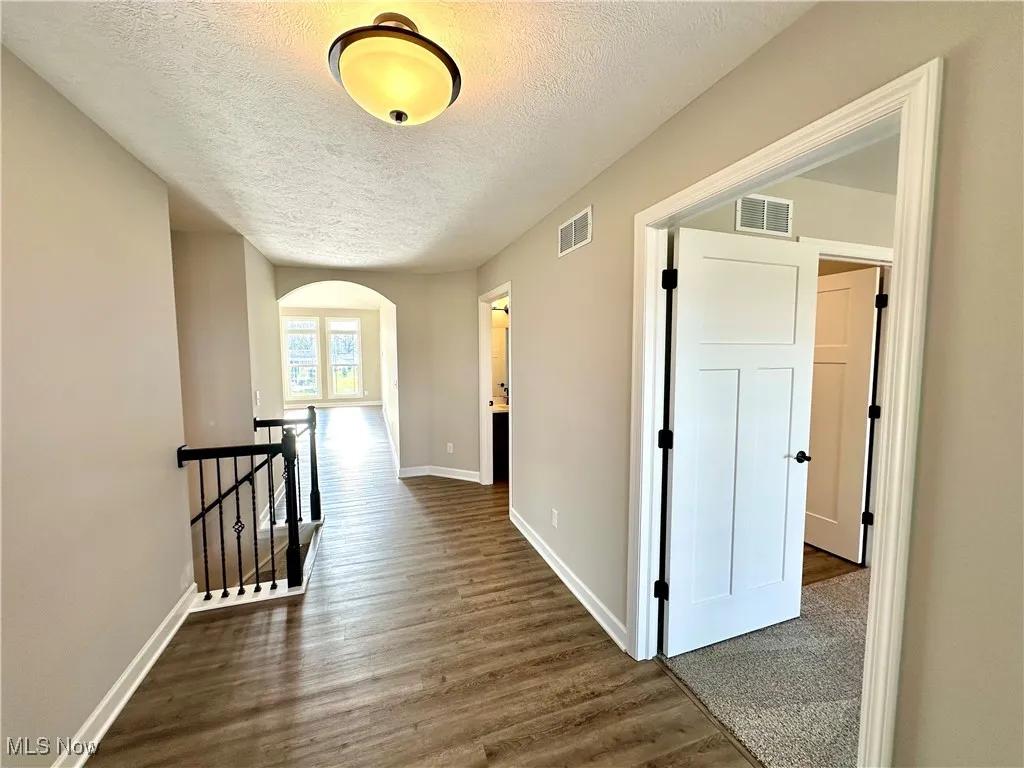 Hall with a textured ceiling and dark hardwood / wood-style flooring
