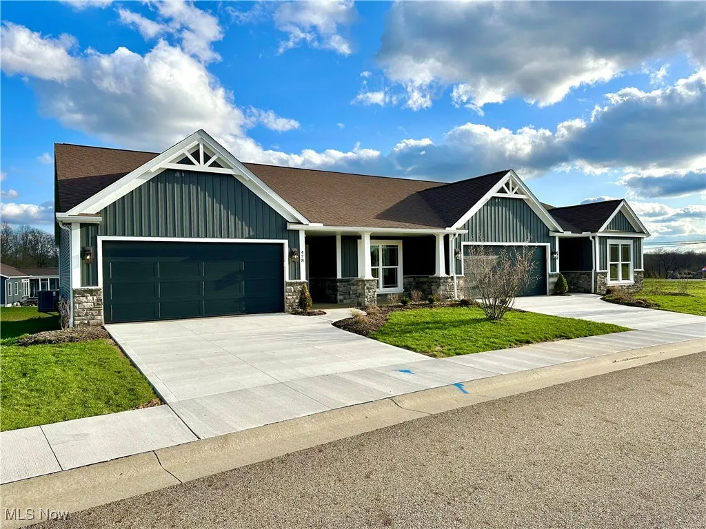 View of front of home with a garage, driveway, stone siding, and board and batten siding