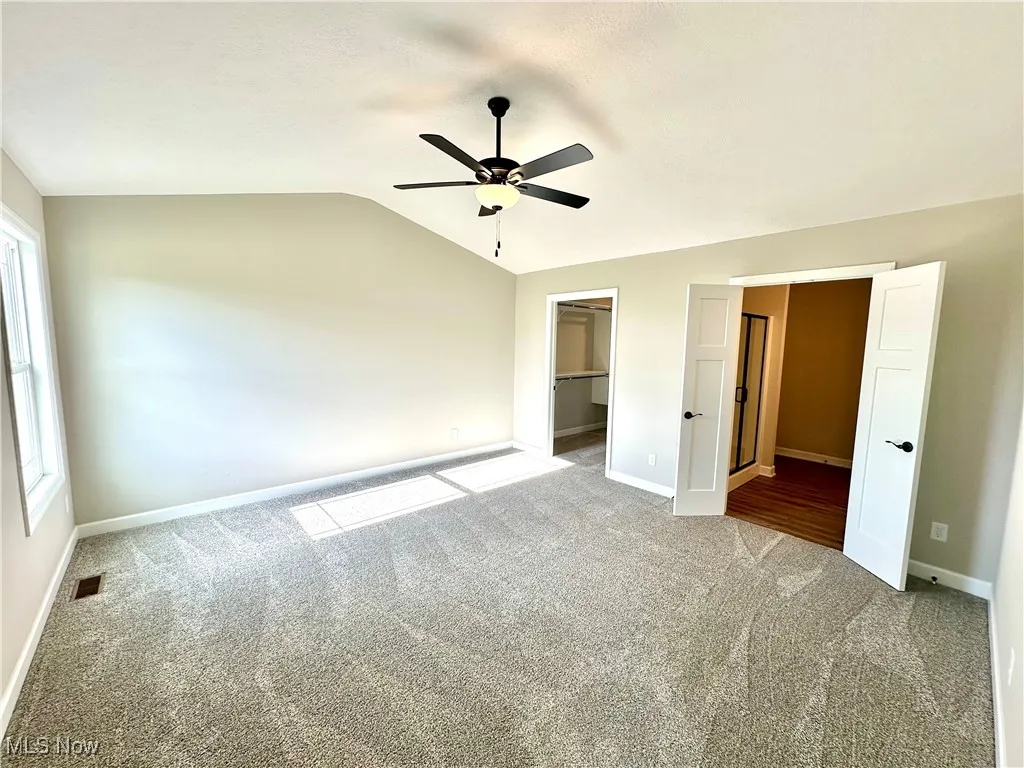 Unfurnished bedroom featuring multiple windows, a walk in closet, vaulted ceiling, and ceiling fan