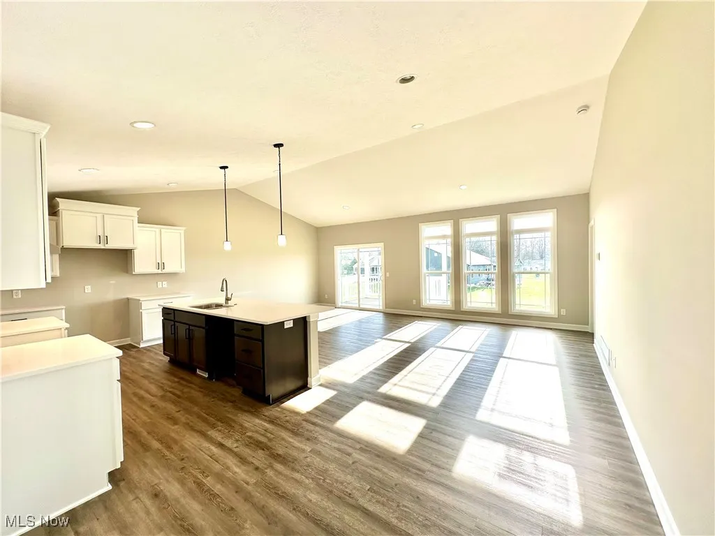 Kitchen featuring sink, vaulted ceiling, hardwood / wood-style flooring, an island with sink, and dark brown cabinetry