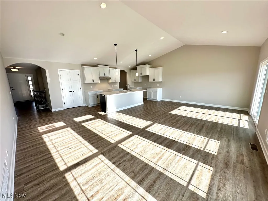 Kitchen featuring dark hardwood / wood-style floors, white cabinetry, hanging light fixtures, lofted ceiling, and an island with sink