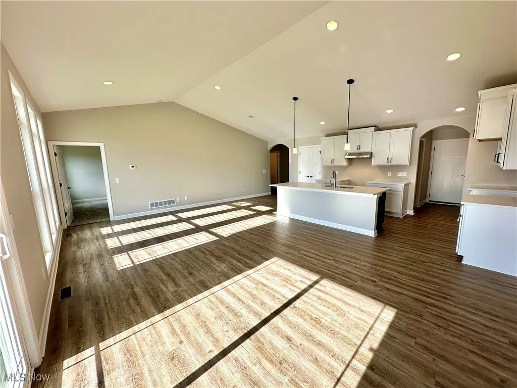 Kitchen featuring white cabinetry, dark hardwood / wood-style floors, an island with sink, decorative light fixtures, and lofted ceiling