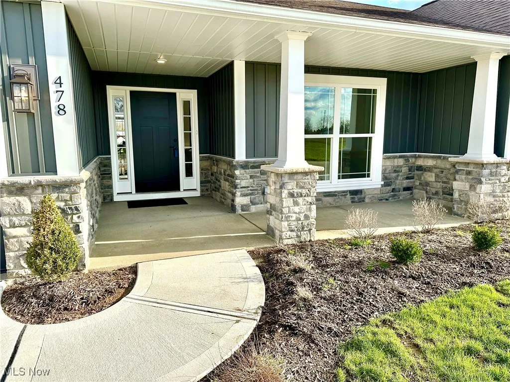 Doorway to property featuring a shingled roof, board and batten siding, covered porch, and stone siding