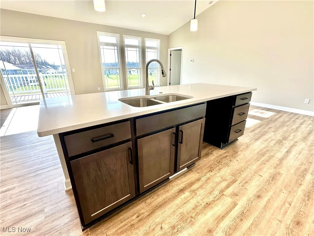 Kitchen featuring sink, a healthy amount of sunlight, pendant lighting, lofted ceiling, and a center island with sink