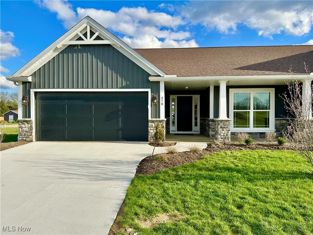 View of front of house with board and batten siding, a front yard, stone siding, an attached garage, and concrete driveway