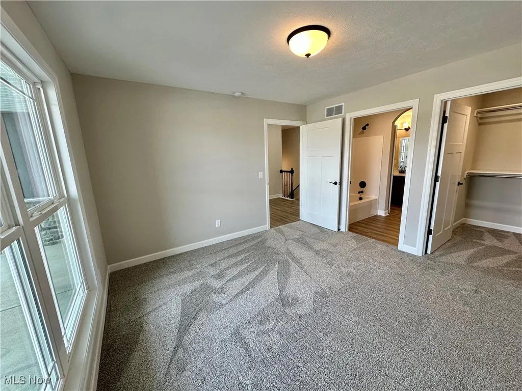 Unfurnished bedroom with carpet flooring, a spacious closet, a textured ceiling, connected bathroom, and a closet