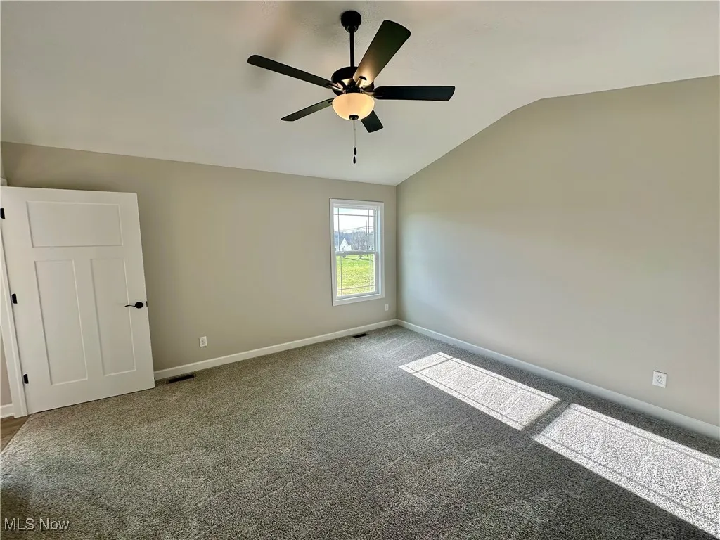 Unfurnished room featuring ceiling fan, carpet, and lofted ceiling